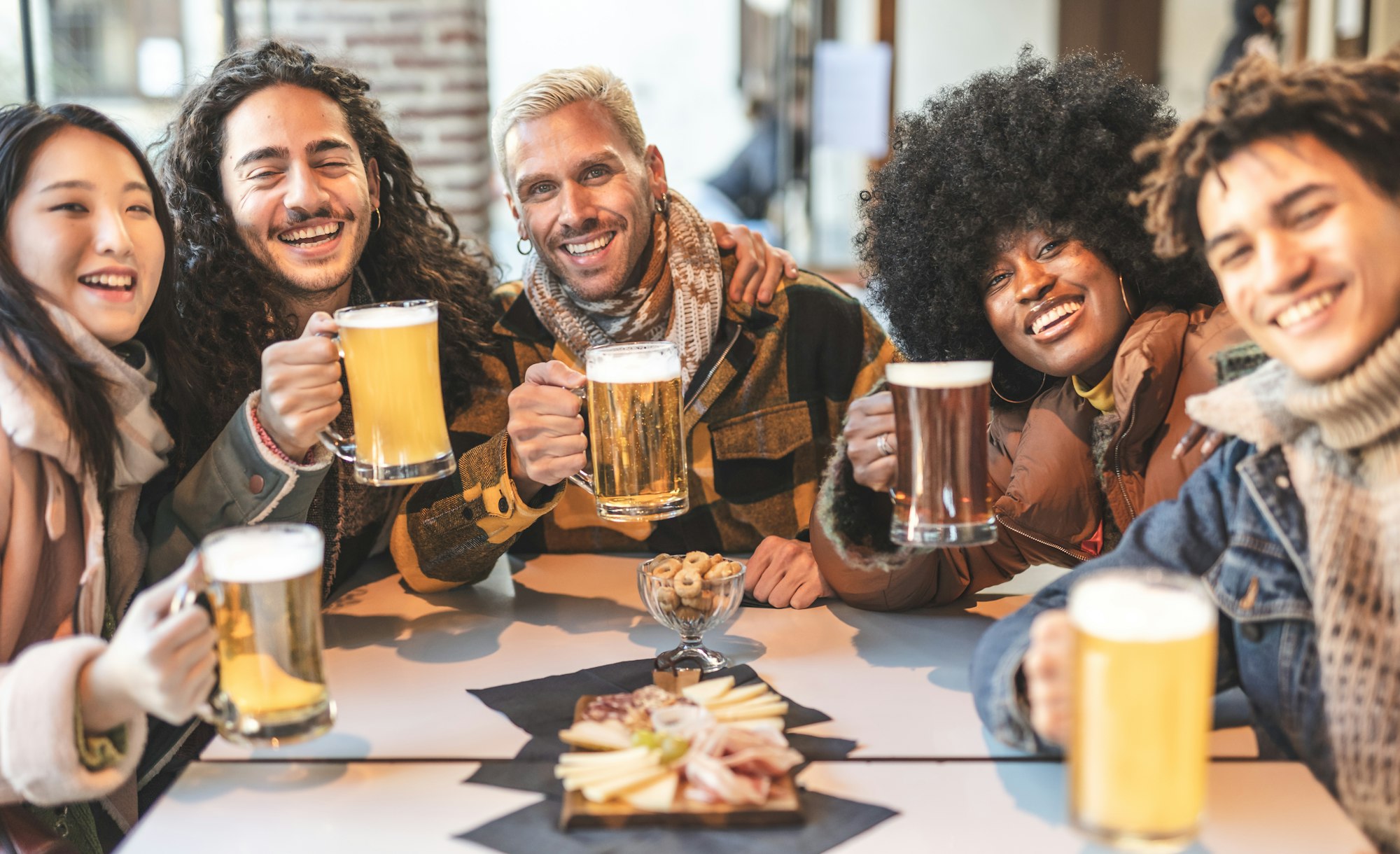 Event Experiences / A group of multiracial friends raise their beer mugs in celebration at a pub event.